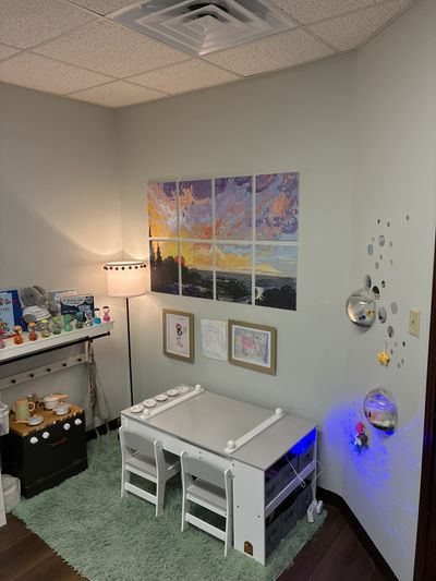 A play corner for younger clients with a small white table, a sunset painting, and a soft lamp