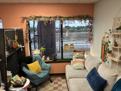 The office sitting area: a teal armchair and gray couch by a window framed with flowering garland